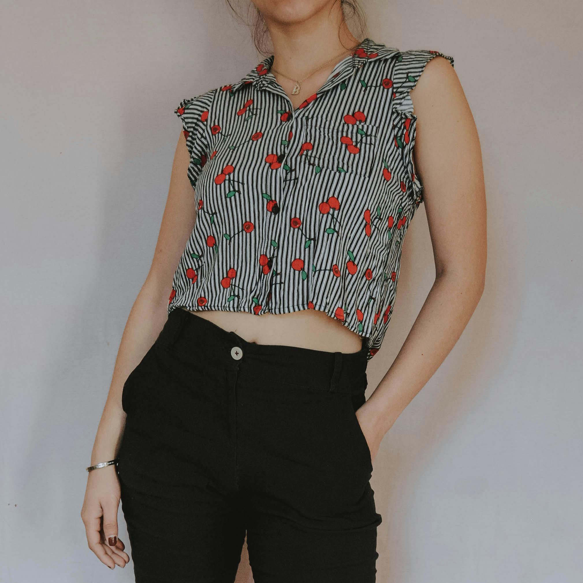 Young woman modeling a cherry print blouse with black pants, showcasing modern casual fashion.